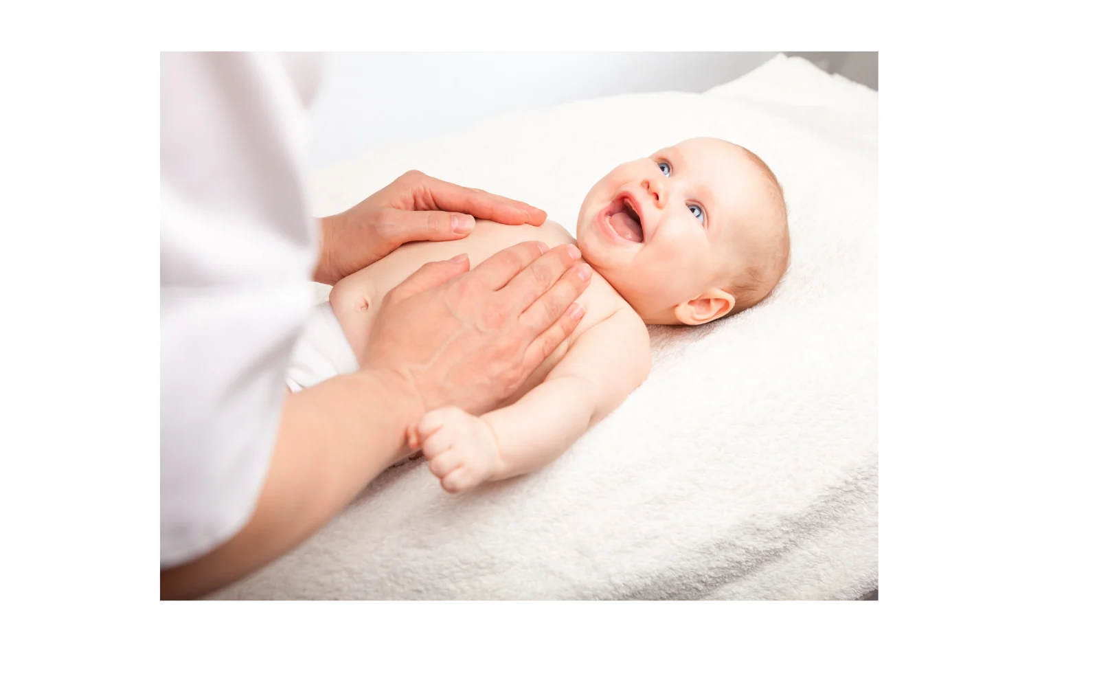 Les mains d’un adulte massent doucement le ventre d’un bébé allongé.
