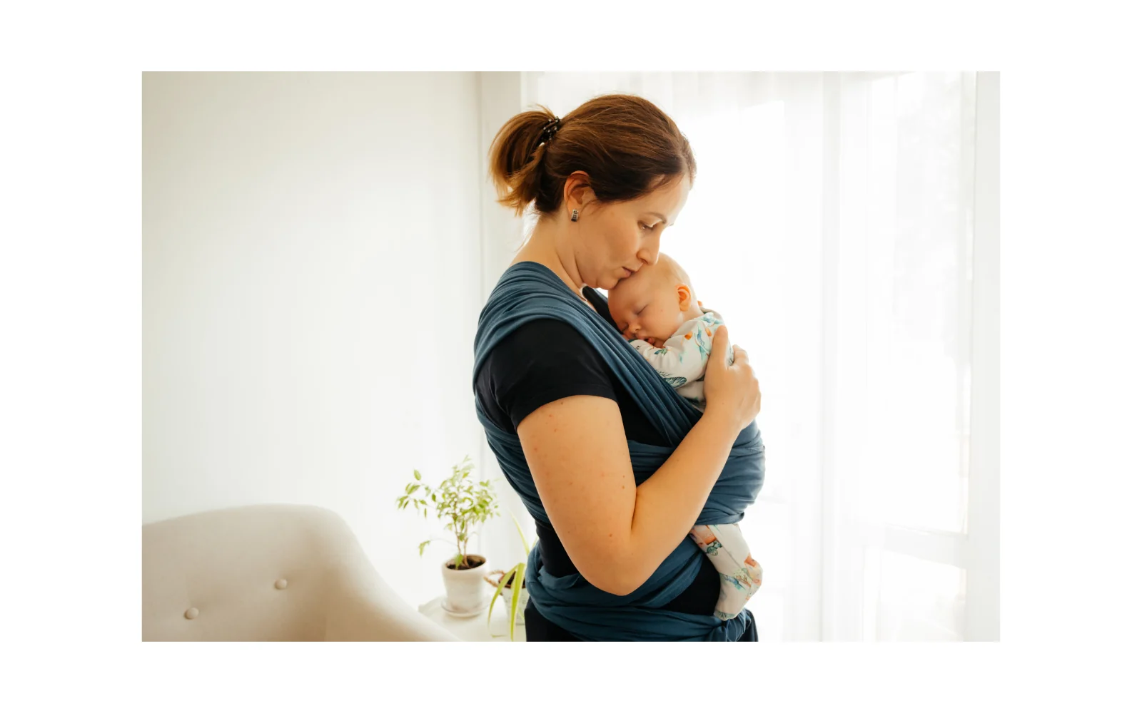 Une femme porte son bébé contre elle dans une écharpe de portage.
